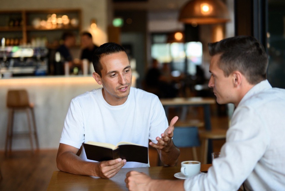 Dos líderes conversando con la Biblia abierta en un café